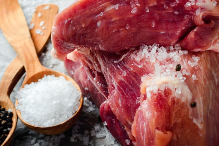 A large piece of fresh juicy meat sprinkled with salt. Preparation of meat for frying steaks.